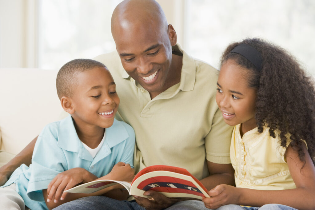 Man and two children sitting in living room reading book and smiling